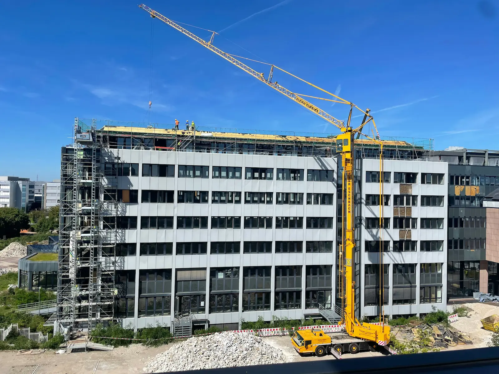 Baukran neben einem modernen Bürogebäude unter Renovierung mit Arbeitern auf dem Dach.