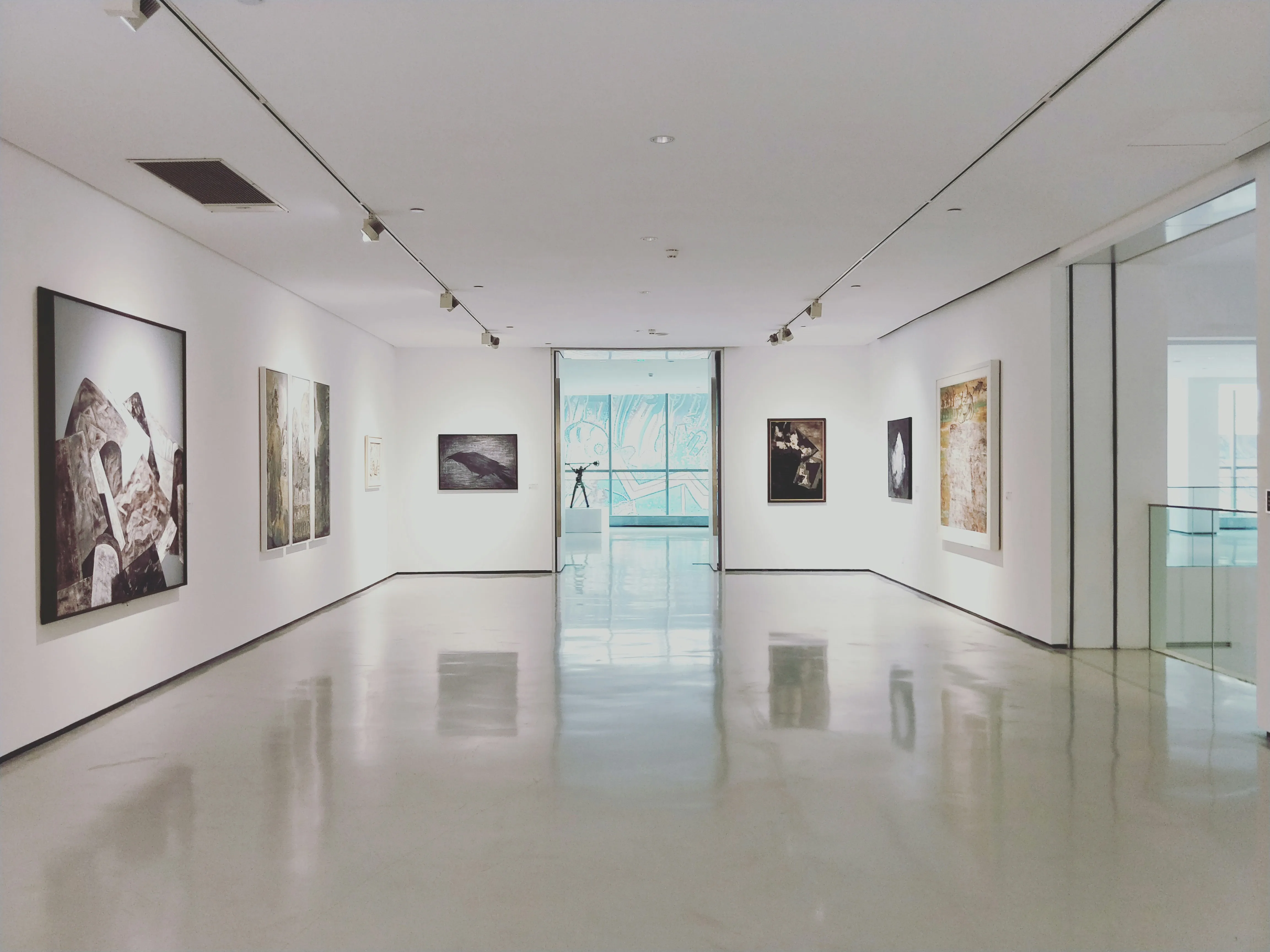 Moderne Kunstgalerie mit weißen Wänden, mehreren gerahmten Gemälden und einer Skulptur in einem hellen Raum.